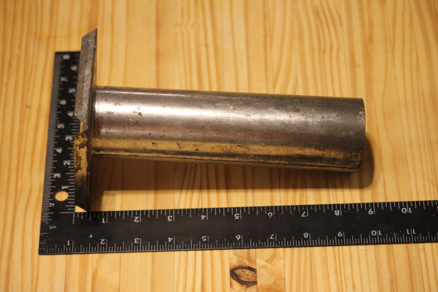 A metal cylindrical pillar mold, shown on a light wood grain background with a black ruler for scale.