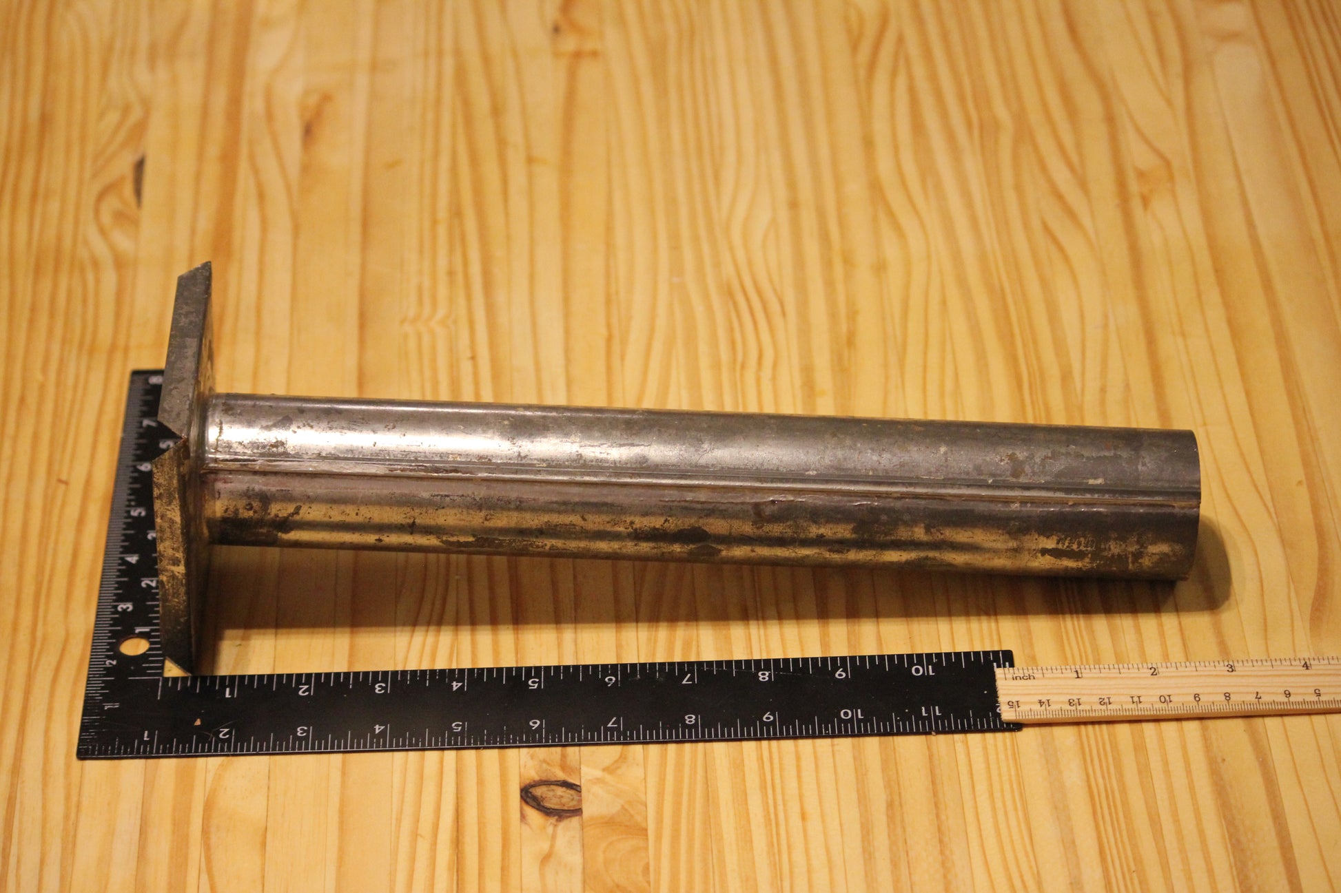 A metal cylindrical pillar mold, shown on a light wood grain background with a black ruler for scale.
