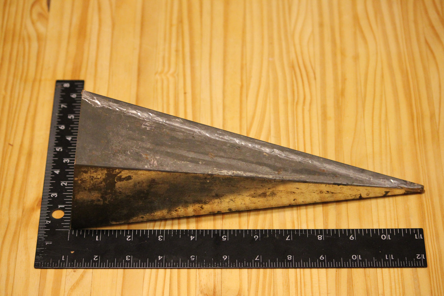 A metal pyramid pillar mold, shown on a light wood grain background with a black ruler for scale.