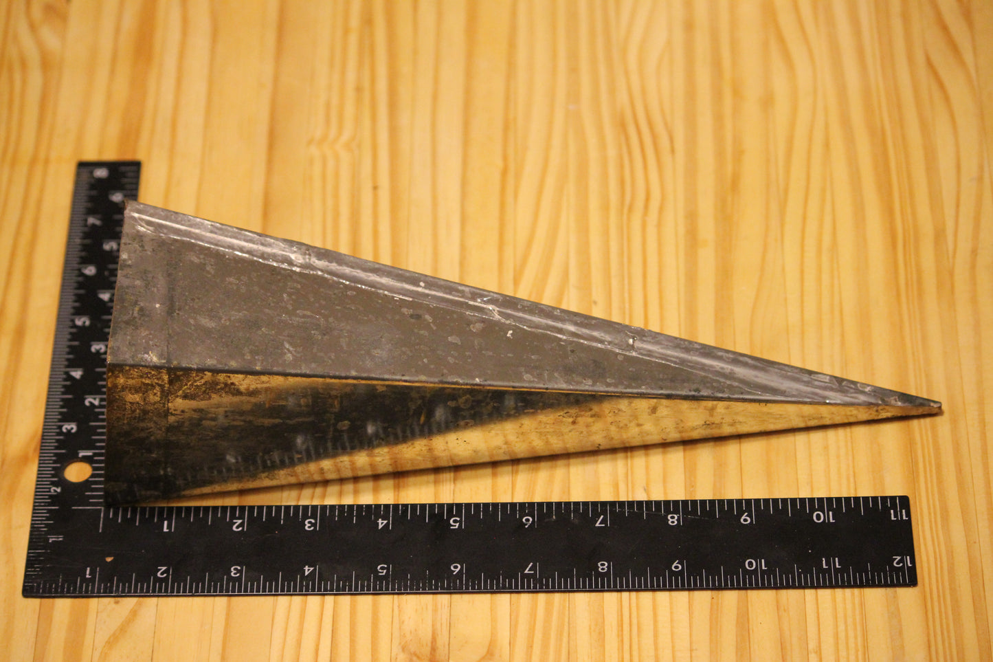A metal pyramid pillar mold, shown on a light wood grain background with a black ruler for scale.