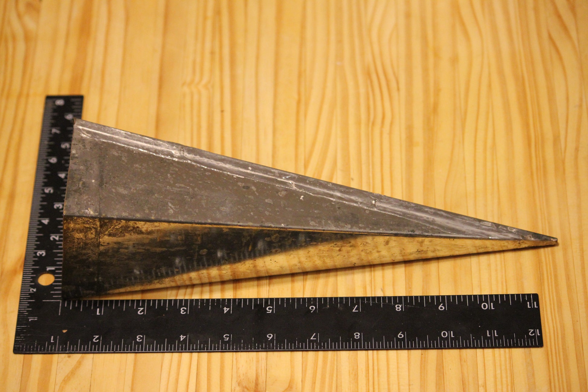 A metal pyramid pillar mold, shown on a light wood grain background with a black ruler for scale.