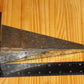 A metal pyramid pillar mold, shown on a light wood grain background with a black ruler for scale.