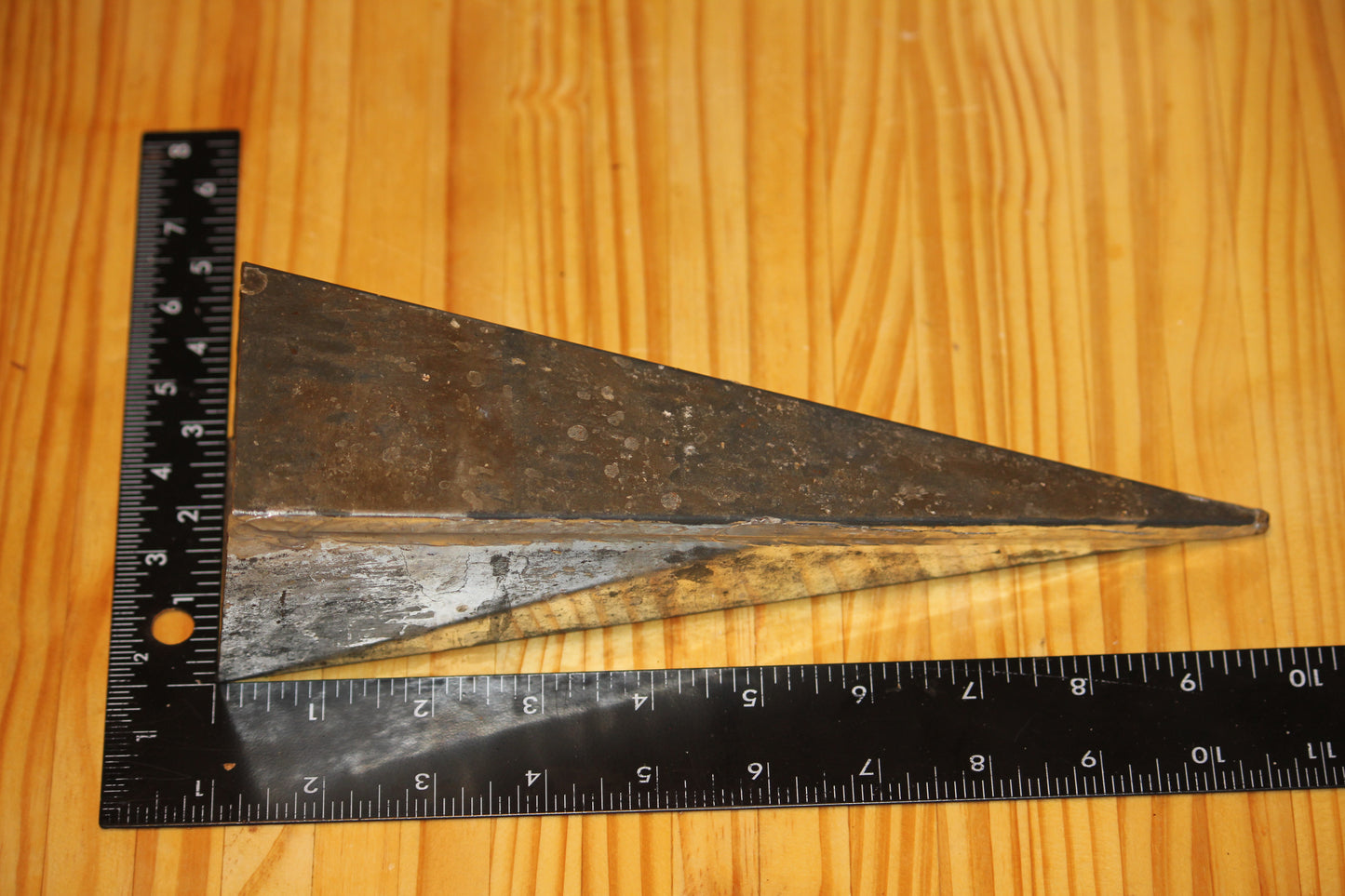 A metal pyramid pillar mold, shown on a light wood grain background with a black ruler for scale.
