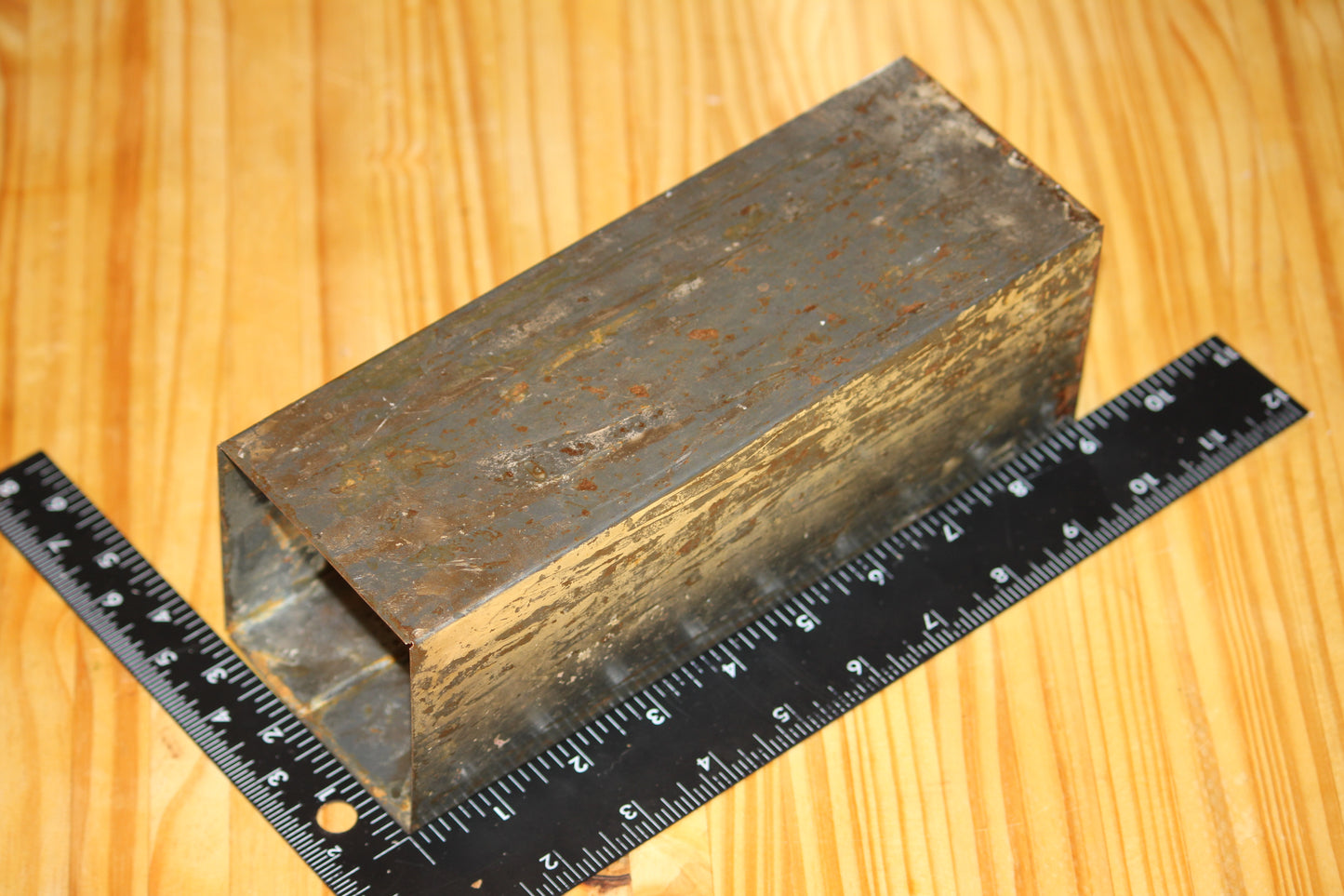 A metal square pillar mold, shown on a light wood grain background with a black ruler for scale.
