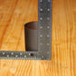 A dark brown candle vessel on a light wood grain surface, with metal rulers placed along the left and right sides to show its height in centimeters and inches.