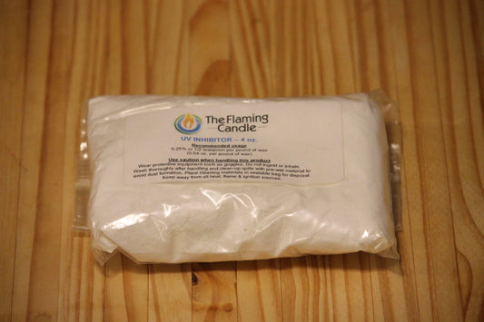 A clear plastic bag containing white powder, labeled 'The Flaming Candle UV INHIBITOR - 4 oz', placed on a light wood grain surface.