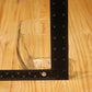 A clear glass candle vessel on a light wood surface with a black L-shaped ruler measuring its height and width.