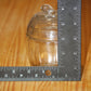 A small clear glass lidded apple jar with a knob on top, shown on a wooden surface with a metal ruler standing vertically and horizontally to indicate its size.