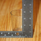 A clear ribbed glass candle vessel, standing on a wooden surface next to a black metal L-square ruler, showing its dimensions against a light wood grain background.