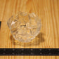 A clear faceted glass candle holder placed on a light wood surface next to a black ruler for scale.