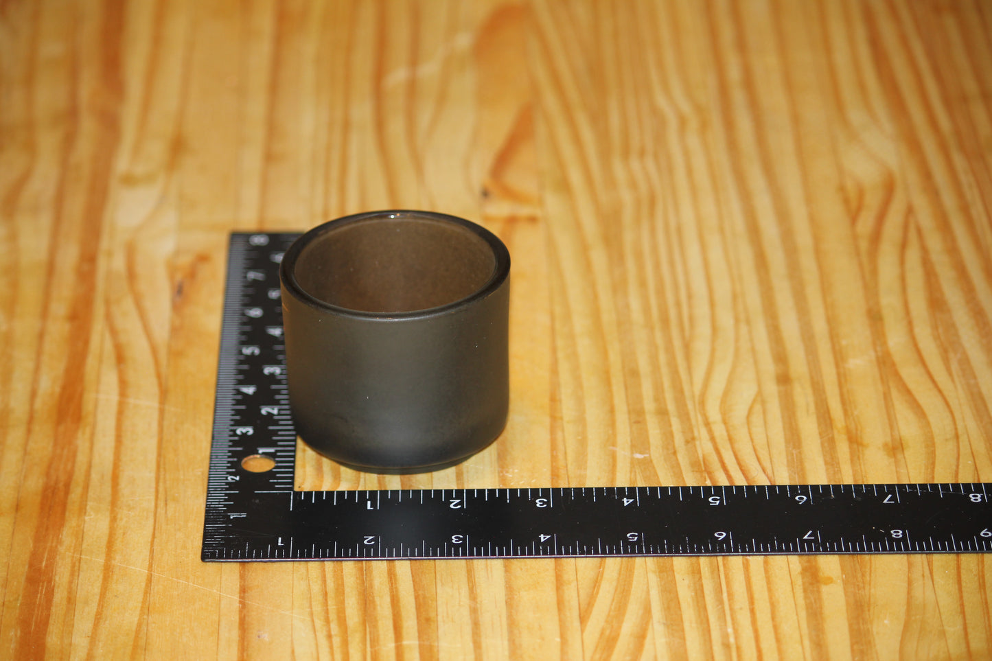 A small matte black cylindrical candle holder placed on a wooden surface next to a black ruler for scale.