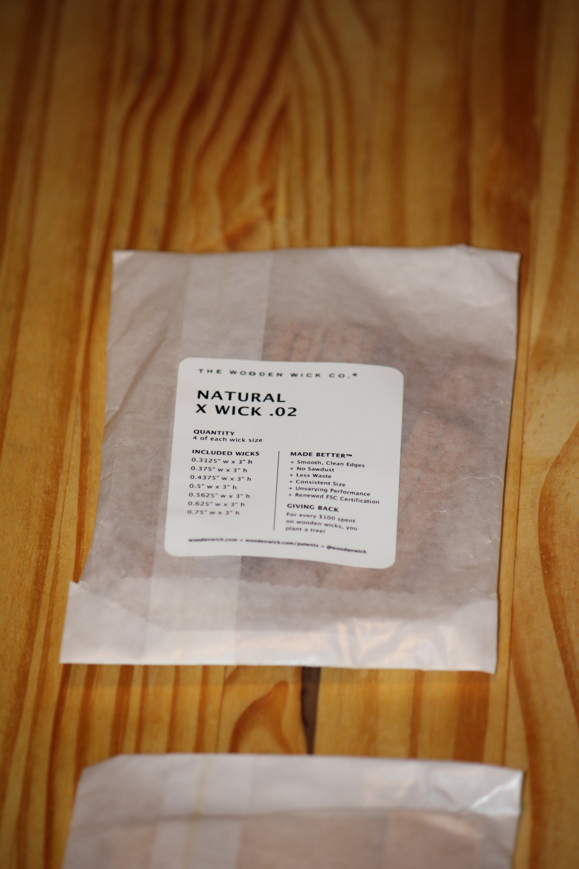 A clear plastic bag containing wood wicks with a white paper label reading 'THE WOODEN WICK CO. NATURAL X WICK .