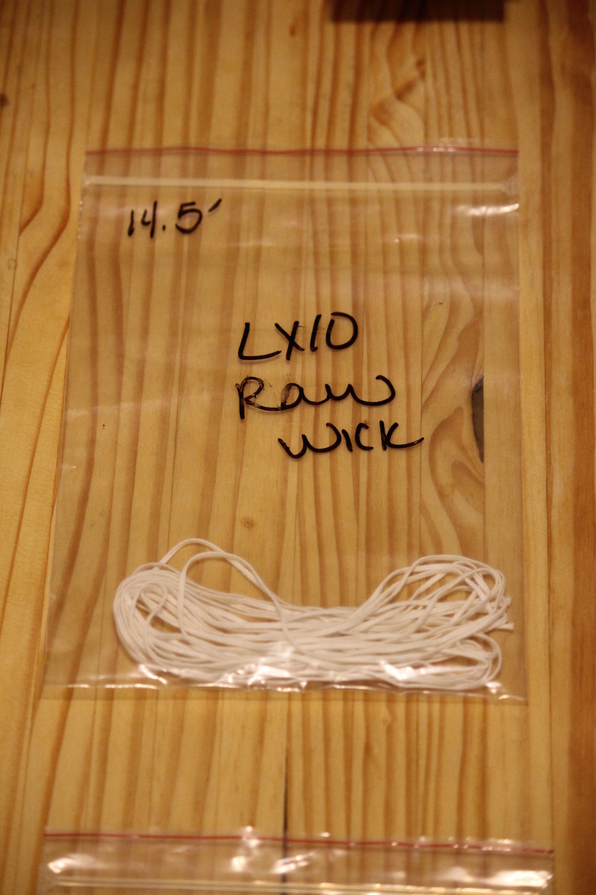 A clear plastic zip-top bag containing a bundle of white wicking material, placed on a light wood surface. 