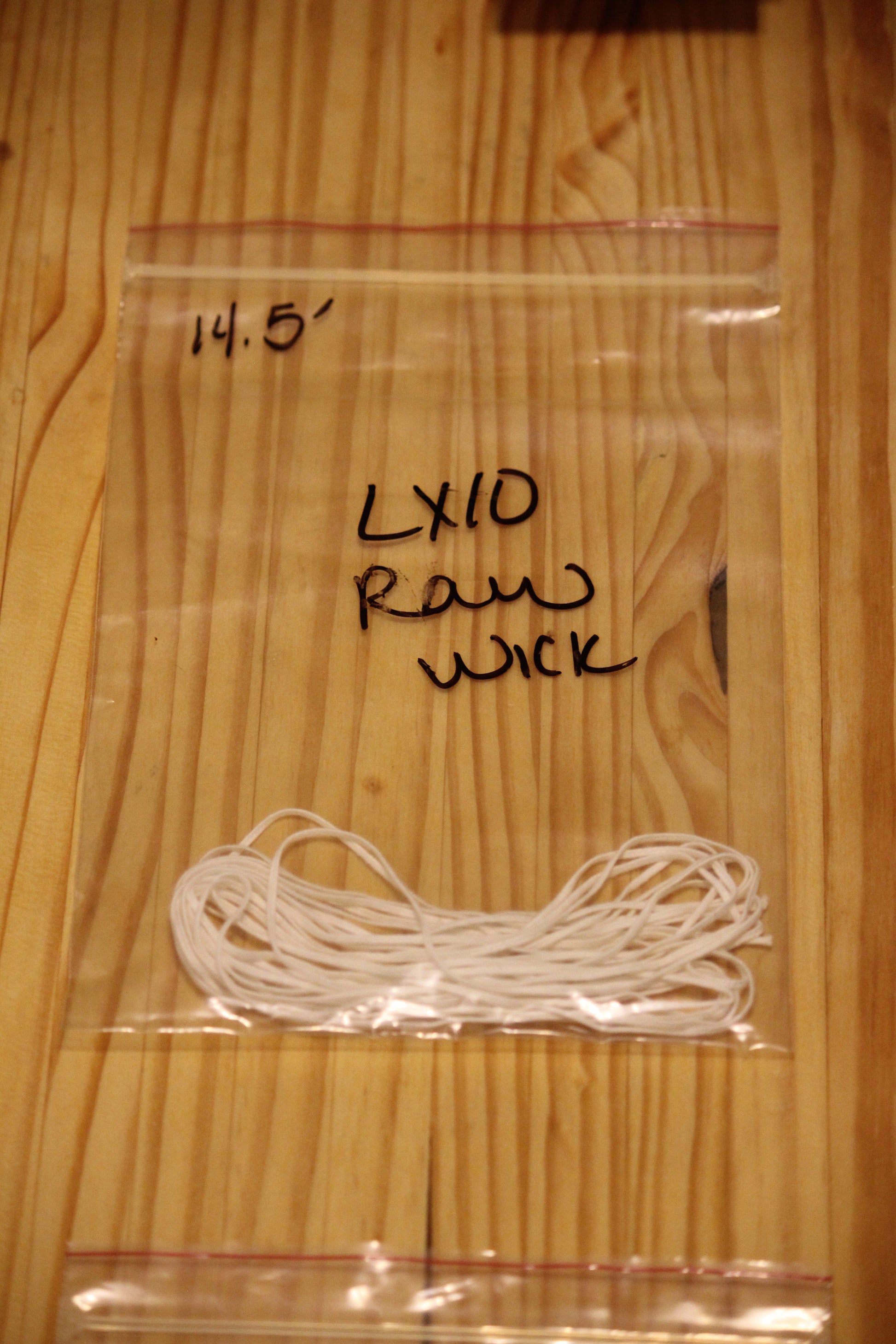 A clear plastic zip-top bag containing a bundle of white wicking material, placed on a light wood surface. 