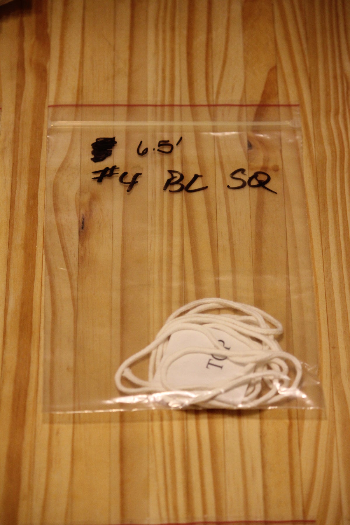 A clear plastic zip-top bag containing a bundle of white wicking material, placed on a light wood surface. 