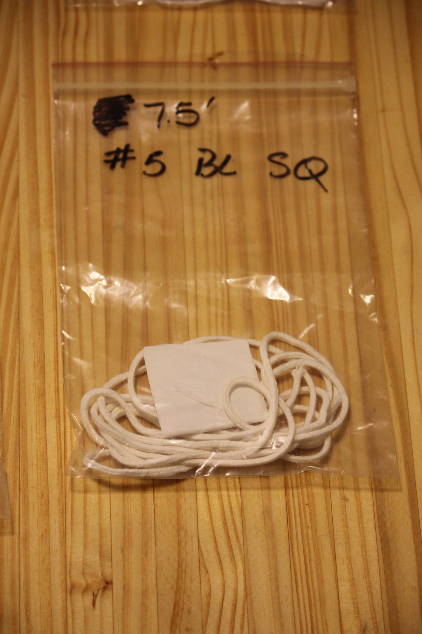 A clear plastic zip-top bag containing a bundle of white wicking material, placed on a light wood surface. 