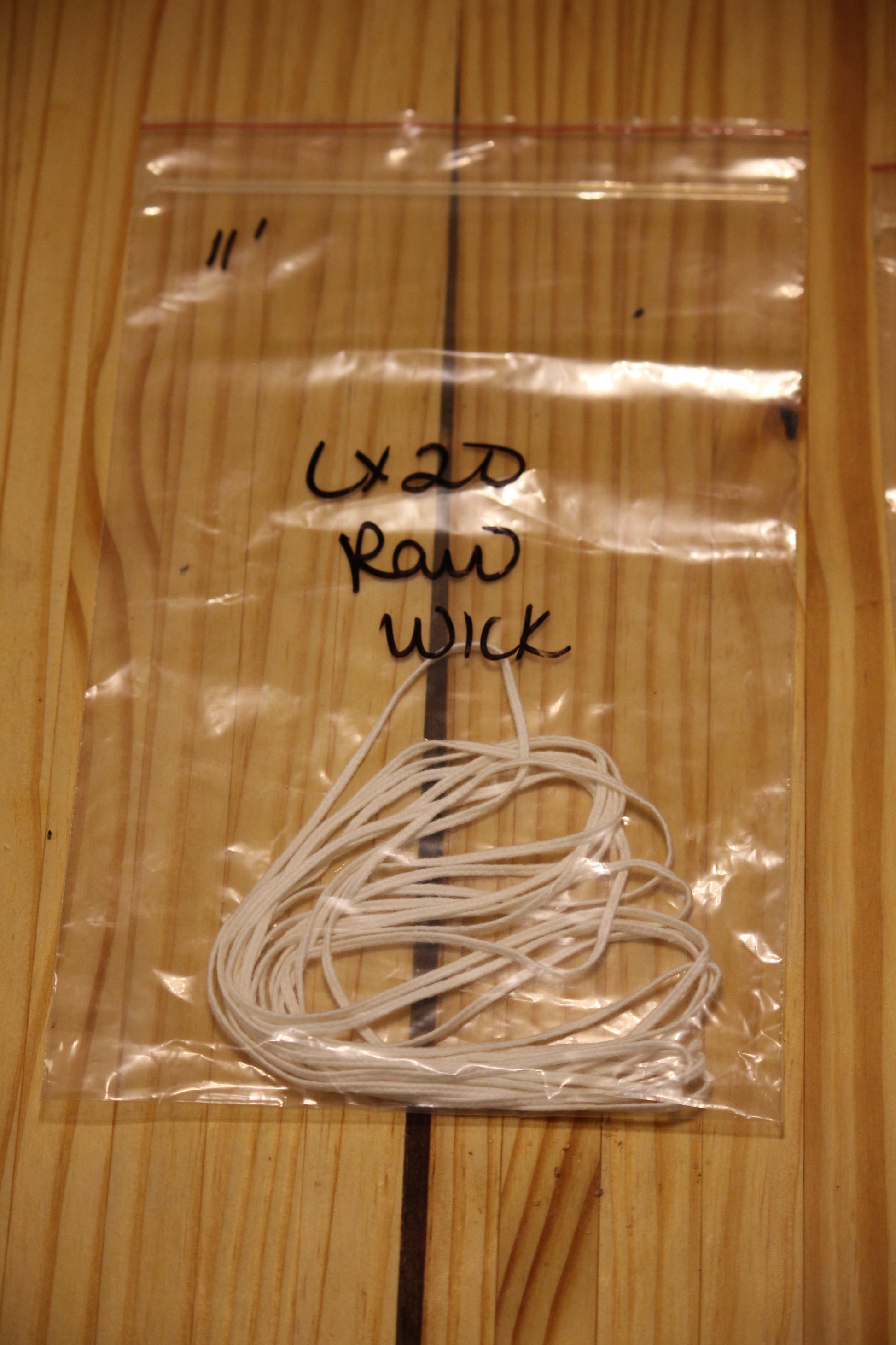 A clear plastic zip-top bag containing a bundle of white wicking material, placed on a light wood surface. 