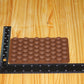 A brown silicone mold with rows of small coffee bean shapes, shown on a light wood surface with black rulers measuring its dimensions.