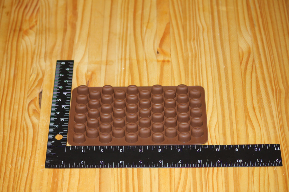 A brown silicone mold with rows of small coffee bean shapes, shown on a light wood surface with black rulers measuring its dimensions.