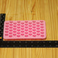 A pink silicone mold with rows of heart-shaped cavities, shown on a light wood surface next to a black ruler for scale.