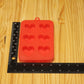 A red silicone mold with six heart-shaped cavities, shown on a light wood grain surface next to a black ruler for scale.