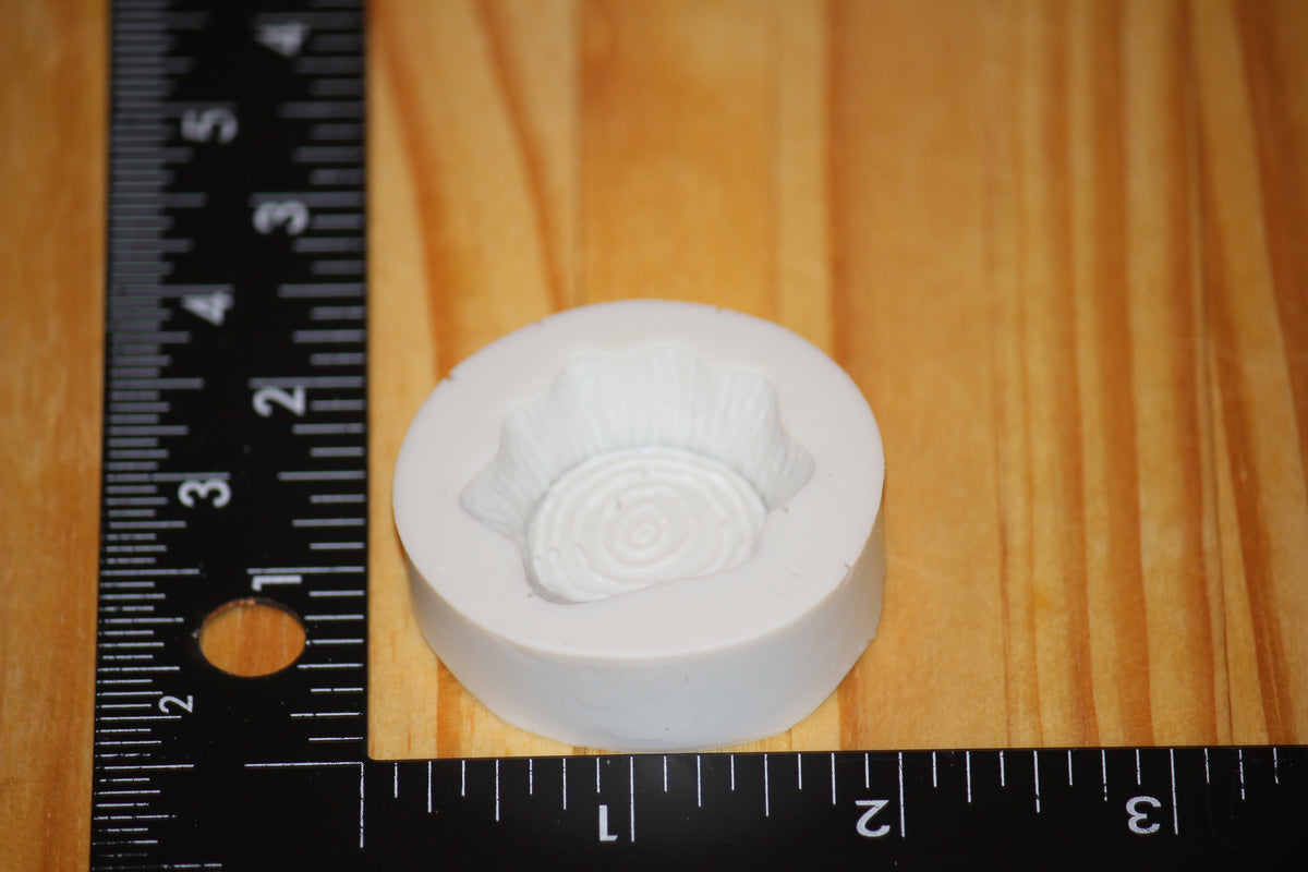 A white circular silicone mold of a wooden stump, shown on a wooden surface next to a black ruler for scale.