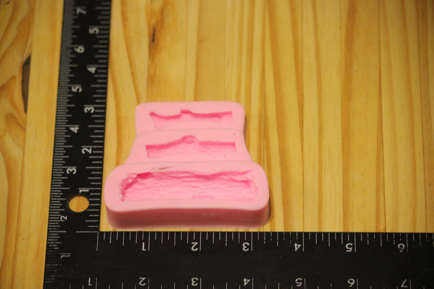 A pink silicone mold of tree branches and sticks, shown on a light wood surface next to a black ruler for scale.