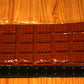A rectangular chocolate mold or tray with a waffle-like raised pattern, sealed in clear plastic packaging and placed on a wooden surface with black measuring rulers along the left and bottom edges for scale.