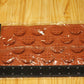 A rectangular brown silicone mold with waffle-shaped cavities, wrapped in clear plastic, shown on a light wood grain surface with a black ruler for scale.