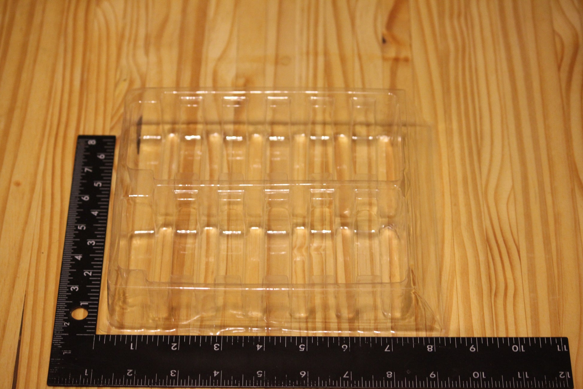 A clear plastic tray with multiple vertical compartments, shown on a light wood grain surface with a black ruler for scale.