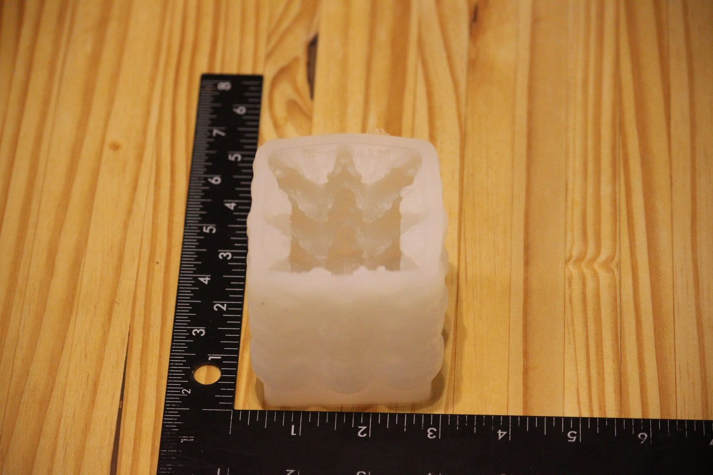 A translucent white silicone mold with a detailed skull design, shown next to a black ruler on a light wood grain background to indicate its size.