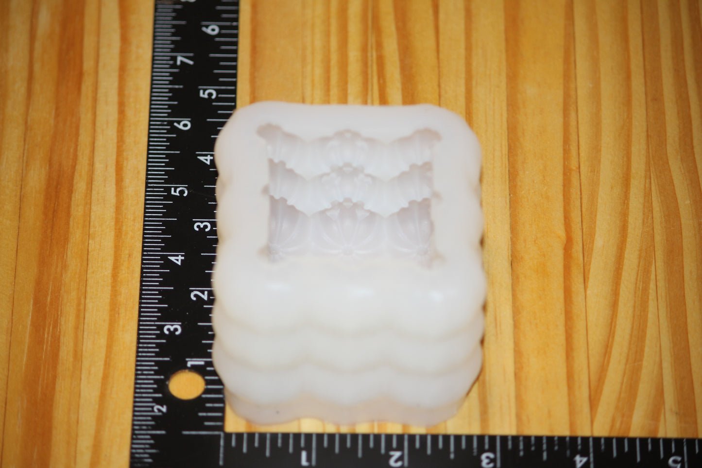 A white silicone mold with a textured, pumkpin pattern, shown next to a black measuring ruler on a light wood grain background.