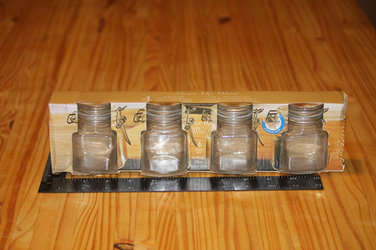 Four small clear glass bottles with clasp caps, shown in their cardboard packaging on a wooden tabletop, with a black ruler placed in front for scale.