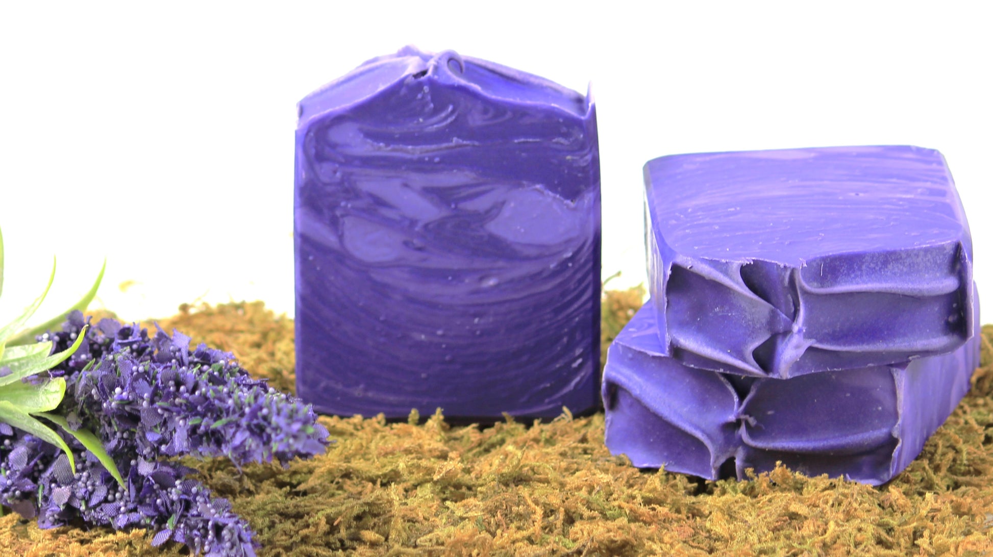 3 handmade soaps with two toned purple swirls on a bed of moss with lavender flowers