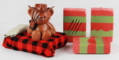 Red and green striped soap bar with 4 slash marks sit next to a bed with a bear with claw hands