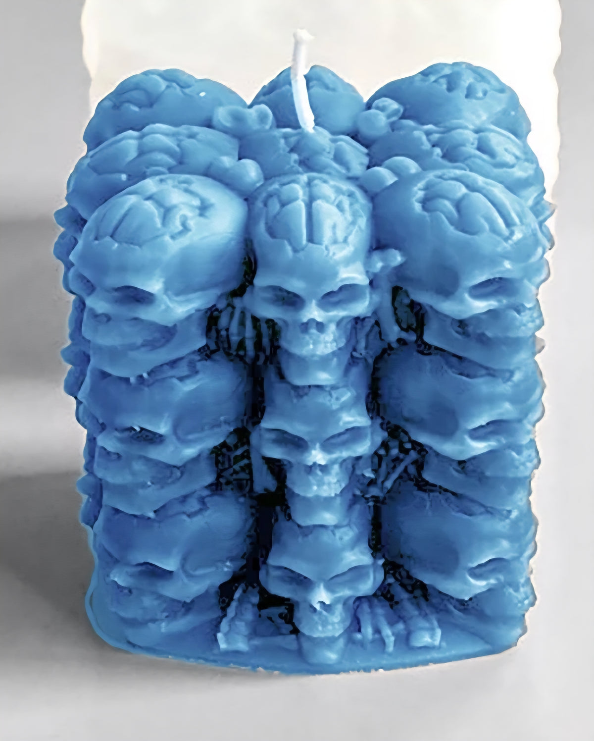 A blue wax candle sculpted with multiple stacked skull and brain-like motifs, shown upright against a plain light background.