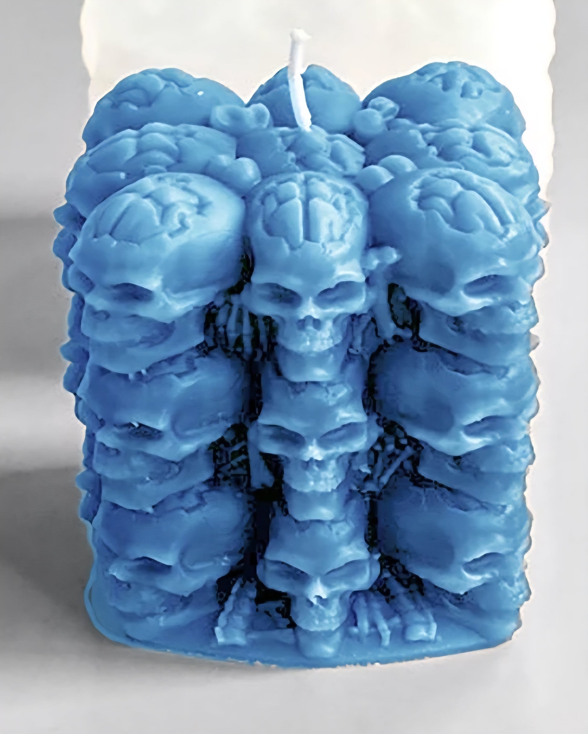 A blue wax candle sculpted with multiple stacked skull and brain-like motifs, shown upright against a plain light background.