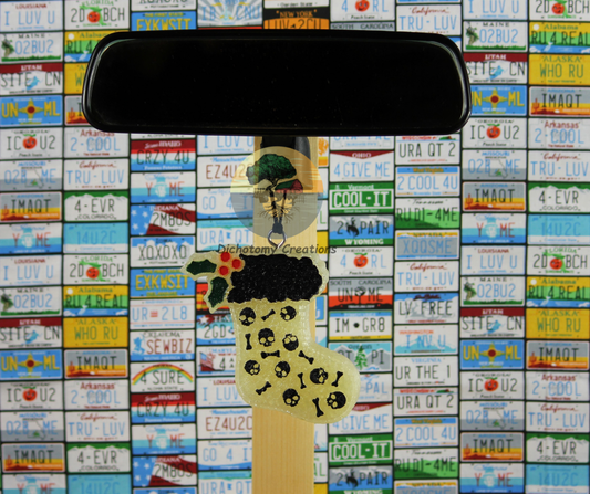 A white christmas stocking freshie with skulls and bones, displayed on a rearview mirror, set against a background of colorful license plates.