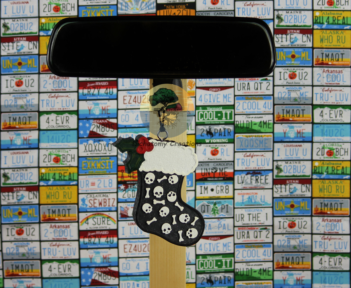 A black christmas stocking freshie with skulls and bones, displayed on a rearview mirror, set against a background of colorful license plates.