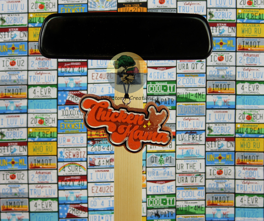 A hanging freshie, brown with orange paint with "Chicken Mama" printed, shown against a background of license plates.