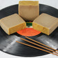 three bars of patchouli scented soap on a vinyl record, accented with incense sticks. 