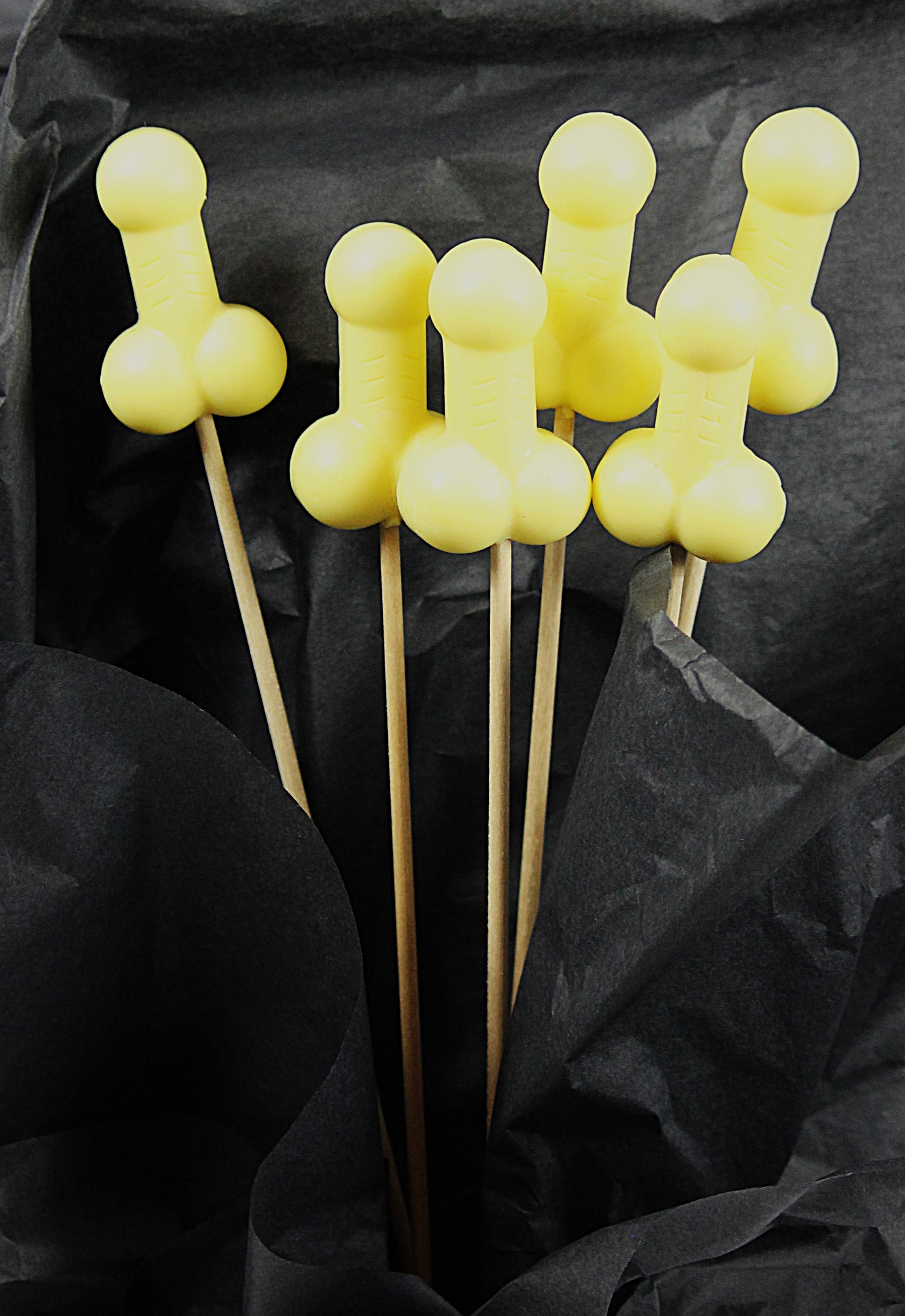 A bouquet of six yellow soap penises against a black backdrop. 