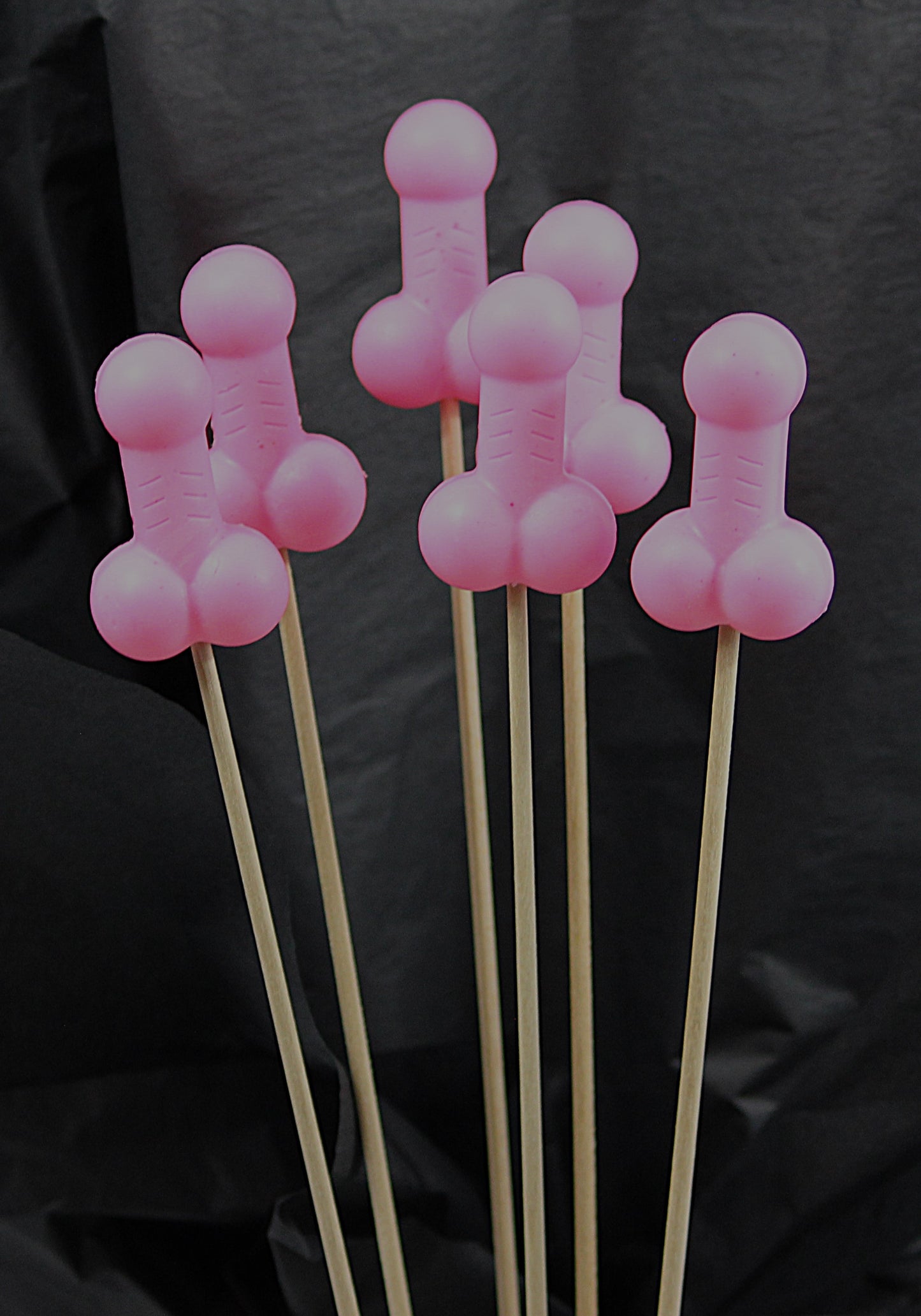 A bouquet of six pink soap penises against a black backdrop. 