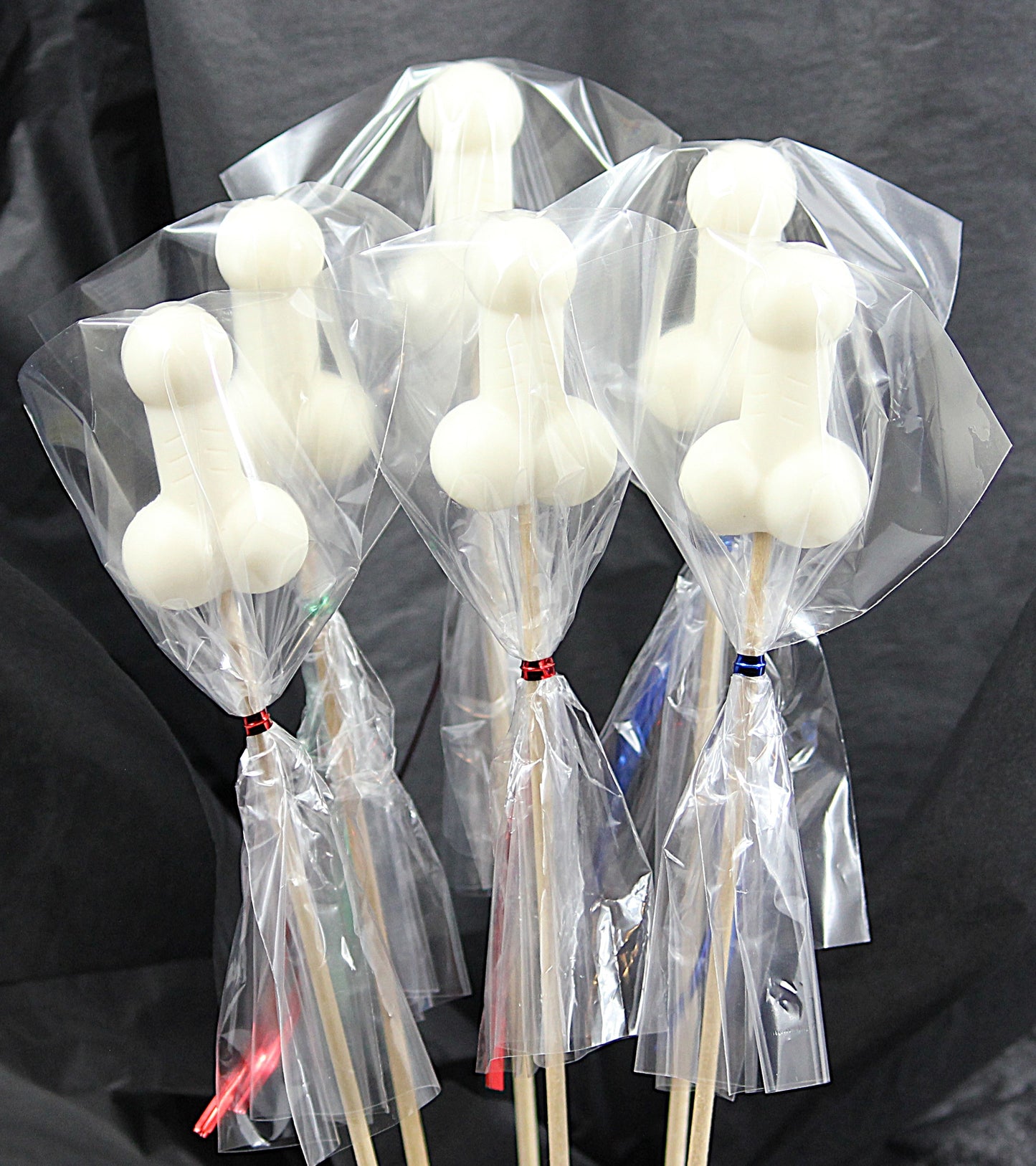 A bouquet of six white soap penises, individually wrapped in clear cellophane, against a black backdrop. 