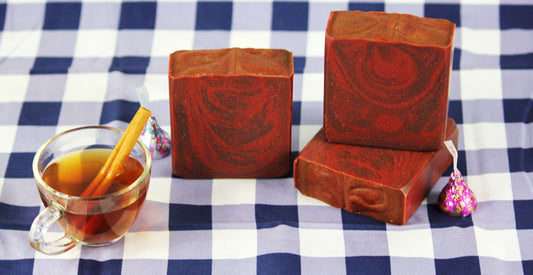 Three bars of soap with a cup of cider on a checkered tablecloth