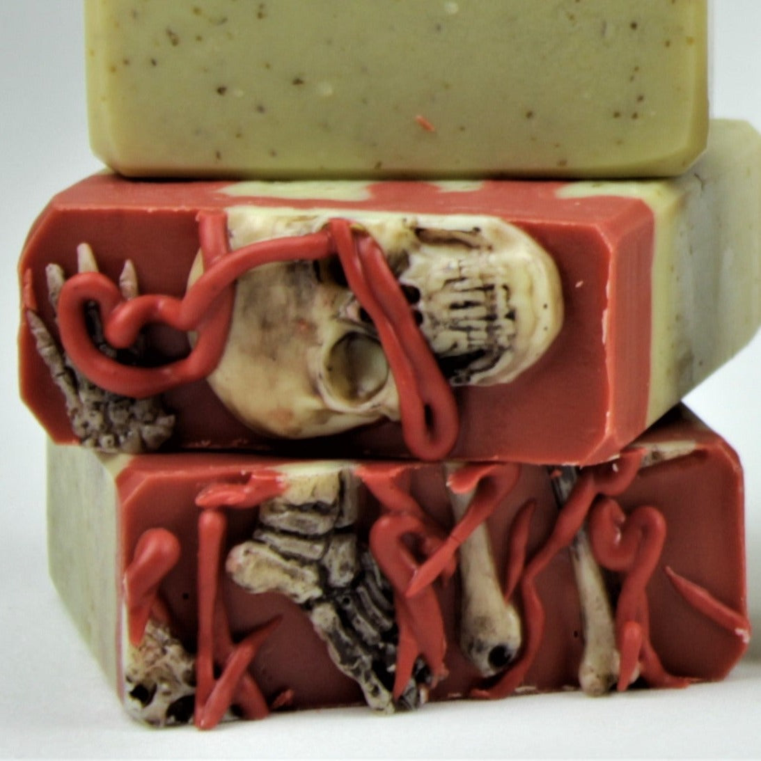 Tops of two bars of Breakfast at Jeff's soaps.  Tops have soap bones on a sea of red soap, and are topped with splattered red soap resembling blood. 